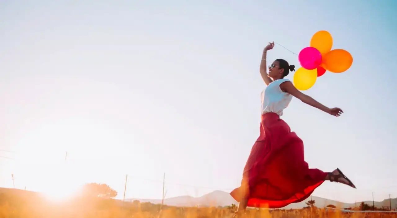 young woman holding balloons and running through a field